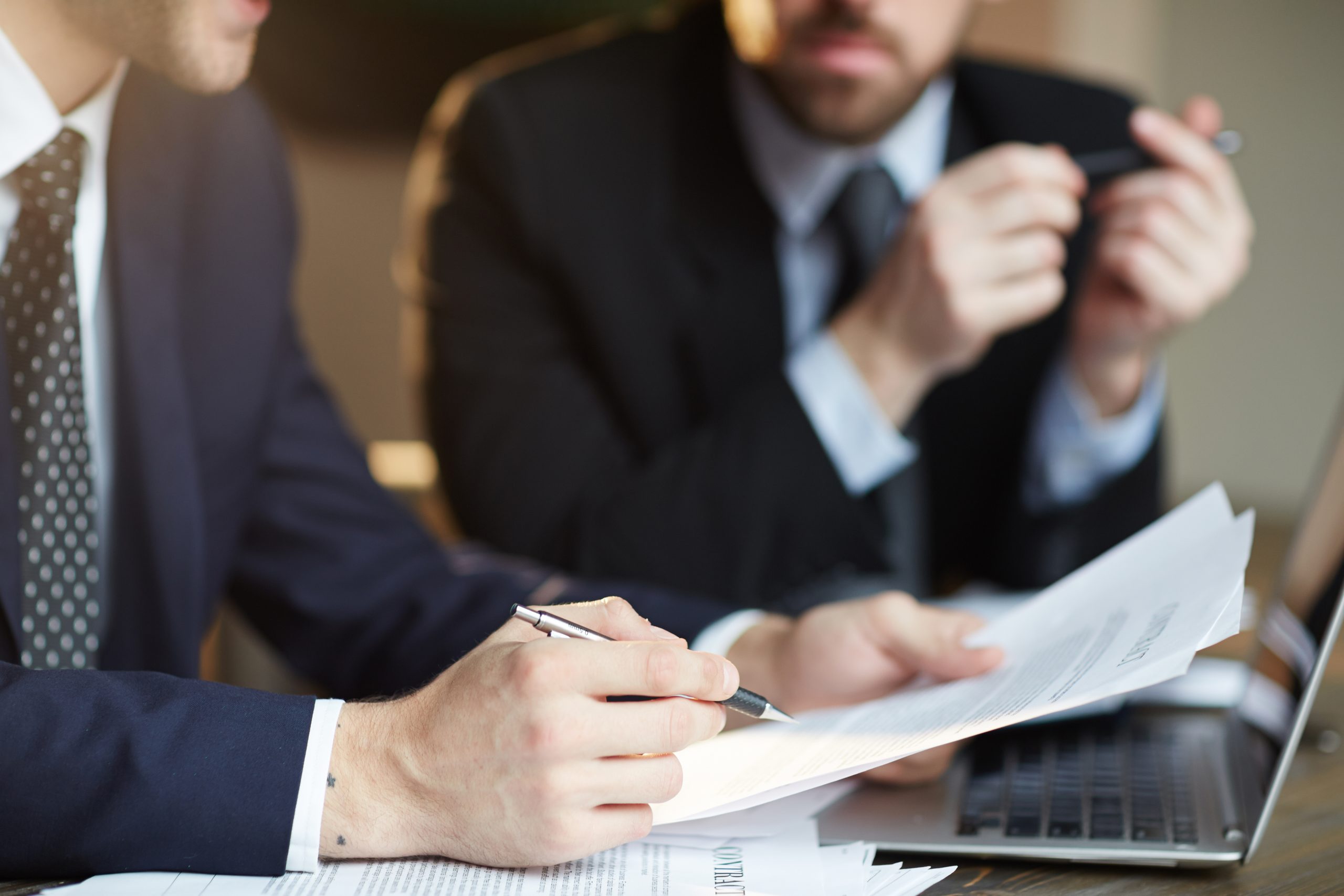 Closeup portrait of two unrecognizable  business partners reviewing paperwork and signing contract papers at table during meeting